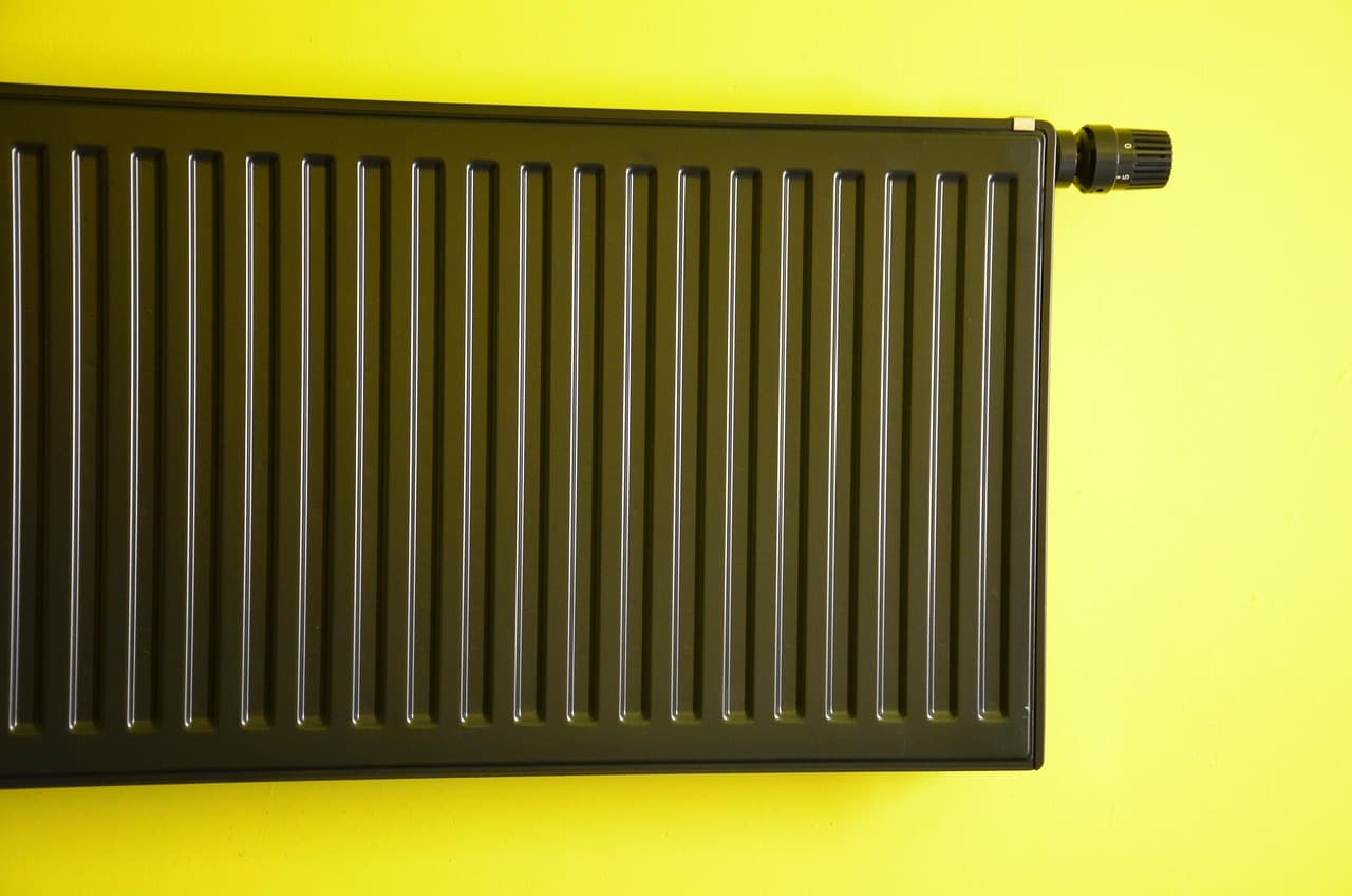 A dark green panel radiator against a mustard yellow wall