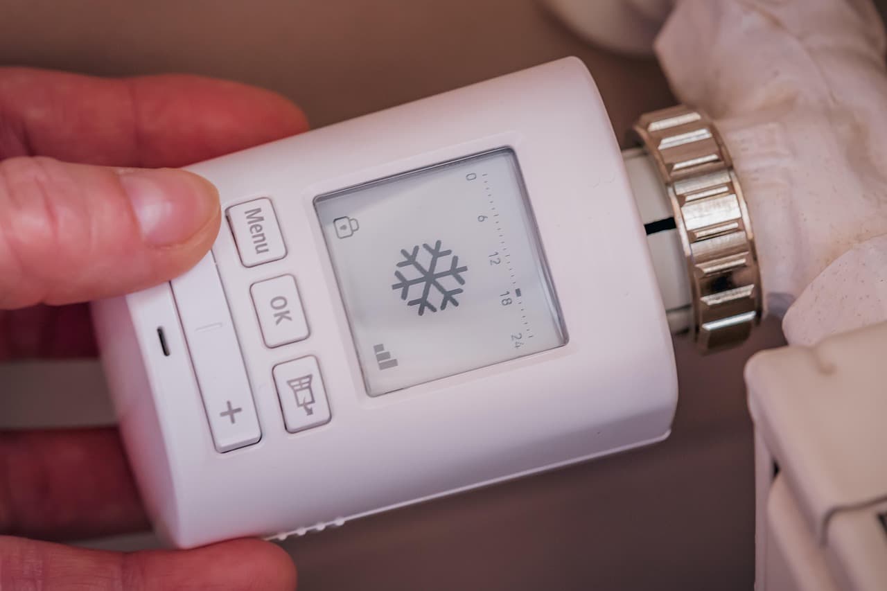 A hand turning a white thermostatic radiator valve set to the frost mark