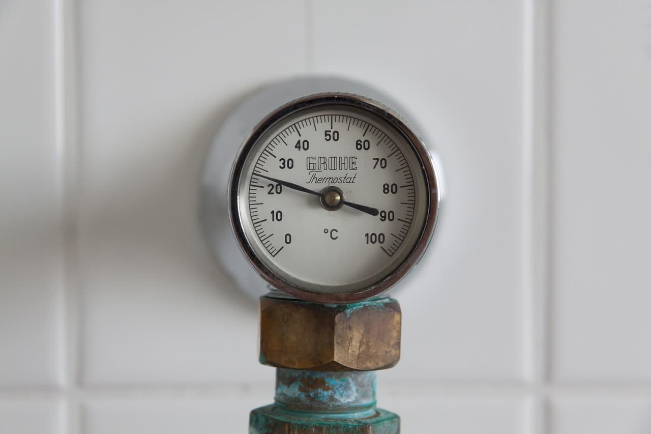 A brass temperature gauge on a pipe against white tiles